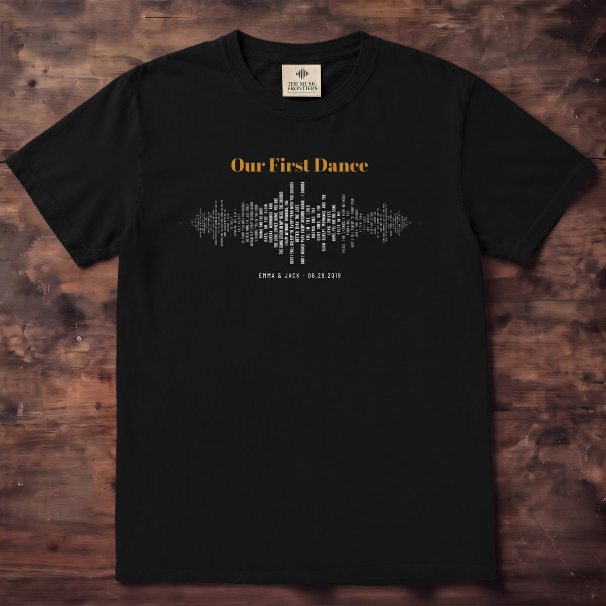 Black tee with a sound wave made of tiny lyric lines and Our First Dance in gold script across it